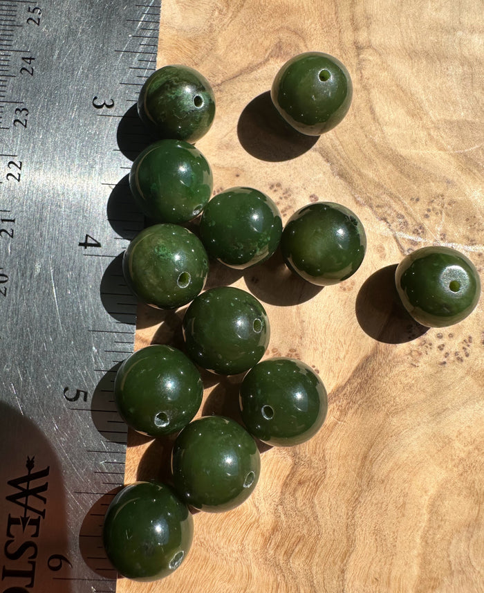 Group of 14mm Cassiar jade beads with drilled holes on a wooden surface