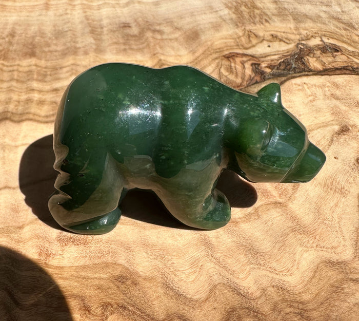 Side view of green jade bear sculpture in a walking pose on a wooden surface