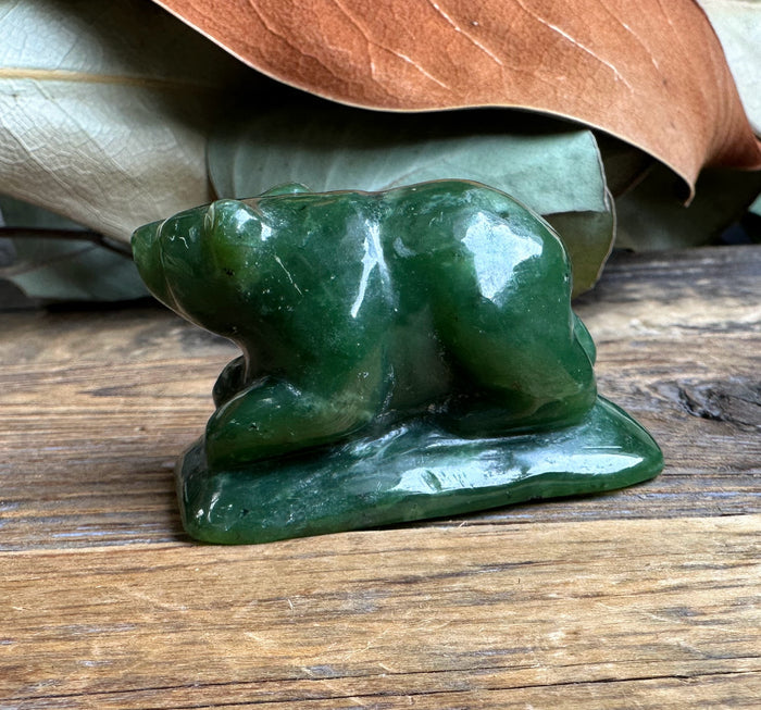 2 inch jade bear figurine in deep green on a weathered wooden surface with dried leaves in the background
