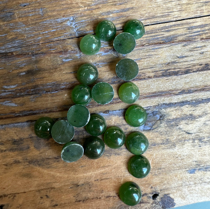 Twenty flat backed round nephrite jade cabochons arranged on a wooden surface.