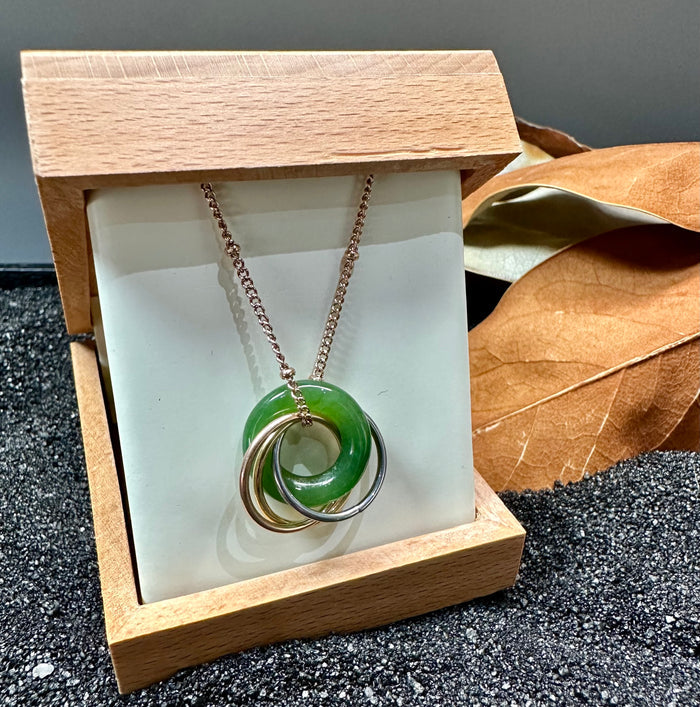 Pendant in a wooden display box showing the green jade donut and layered interlocking rings from a front angle.
