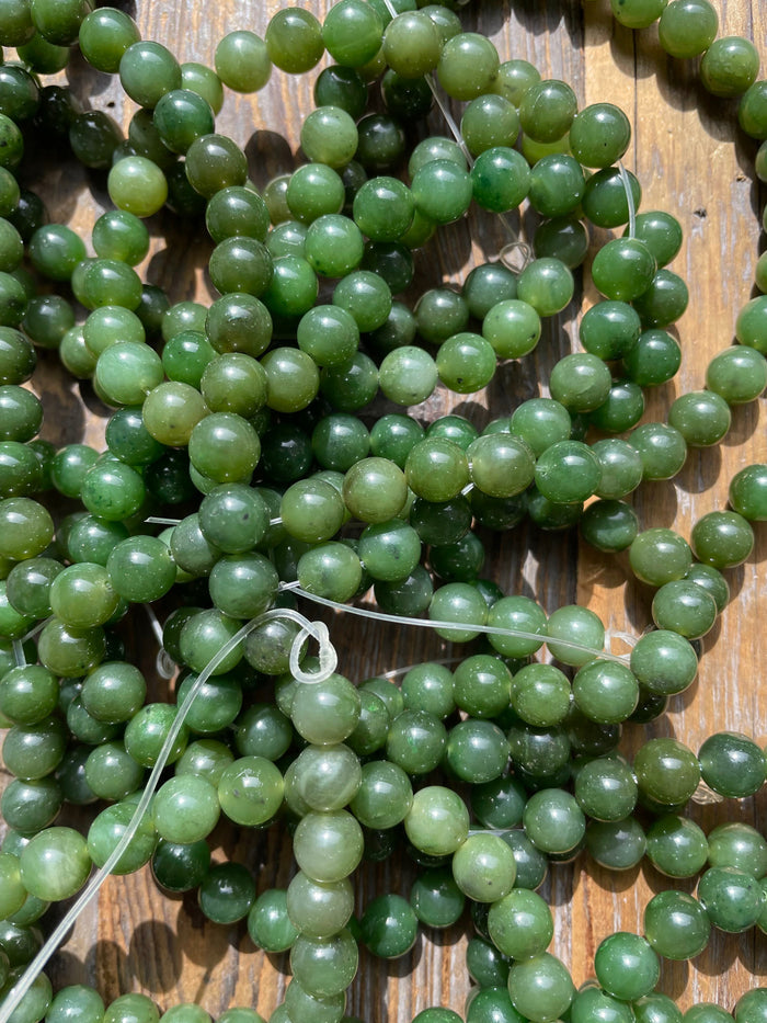 Close up of green 8mm carving grade Canadian jade beads scattered on a wooden surface