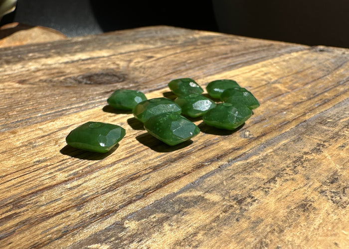 Several faceted green jade beads with holes for stringing spread on a wooden surface