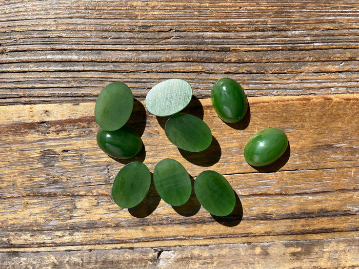 Group of oval green jade cabochons 18x13mm on a weathered wooden surface.