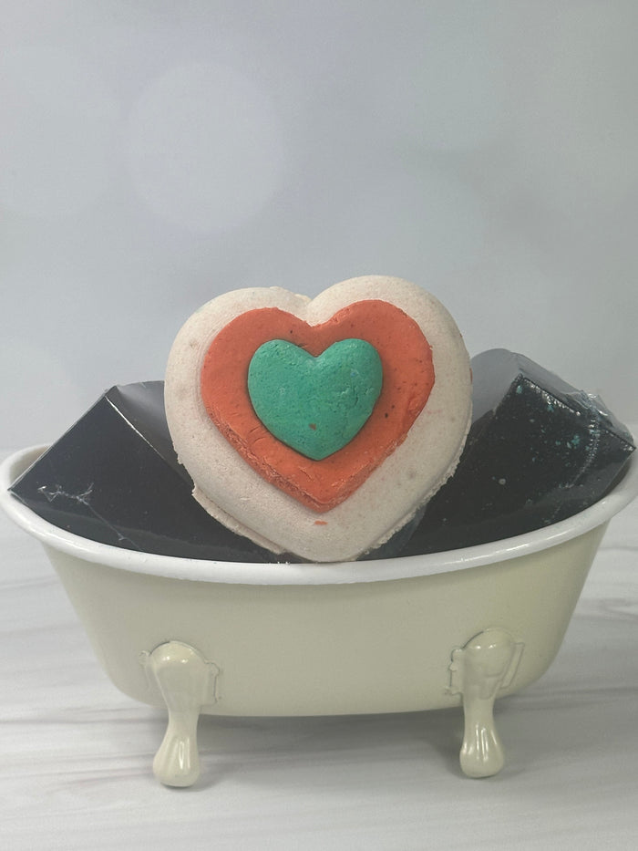 A white orange and turquoise heart shaped bath bomb sitting in a small white bath tub