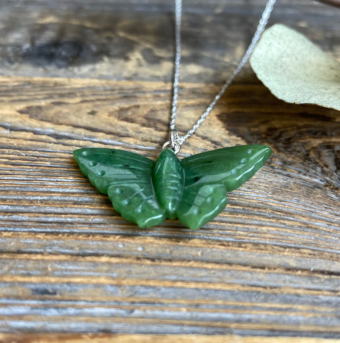 Green butterfly pendant on a silver chain resting on a textured wooden surface.