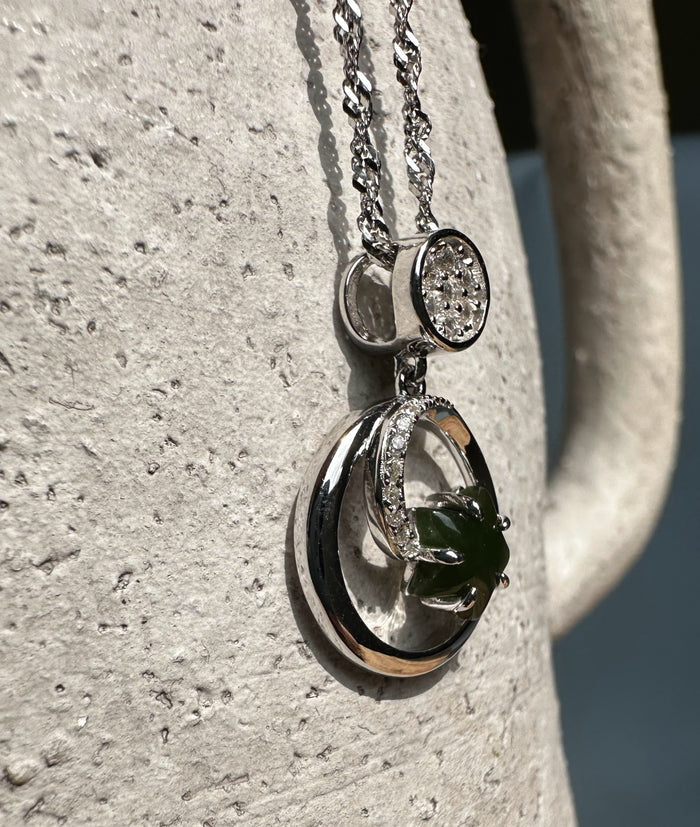 Close up of the silver pendant showing a pavé diamond disk, a crescent with crystals, and a green jade star inside a circular hoop