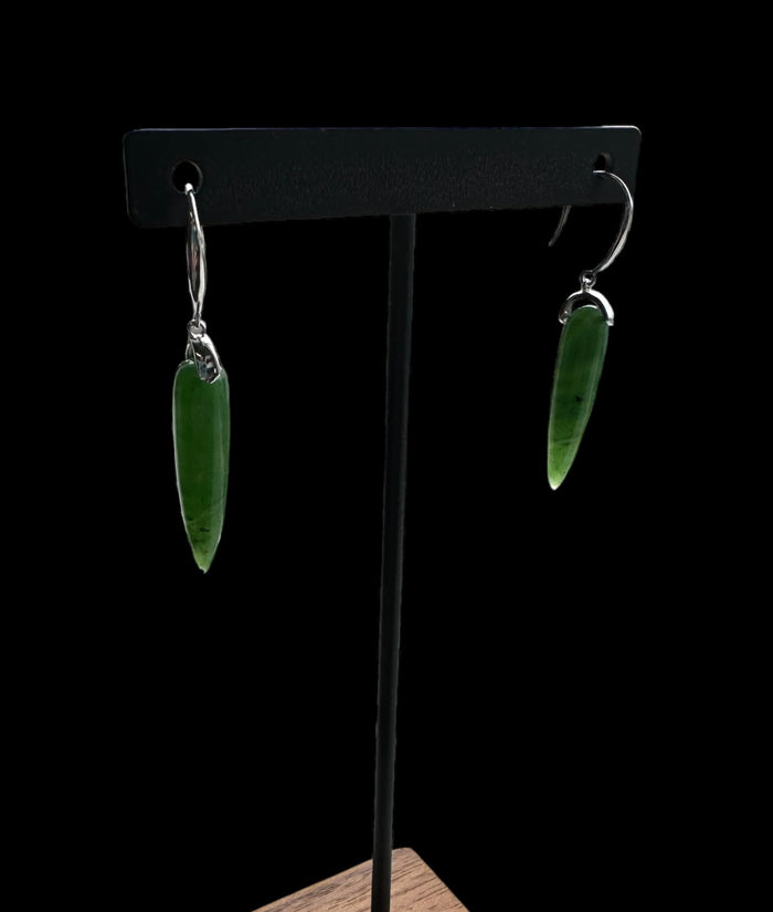 Green jade drop earrings with silver hooks hanging from a black display stand.