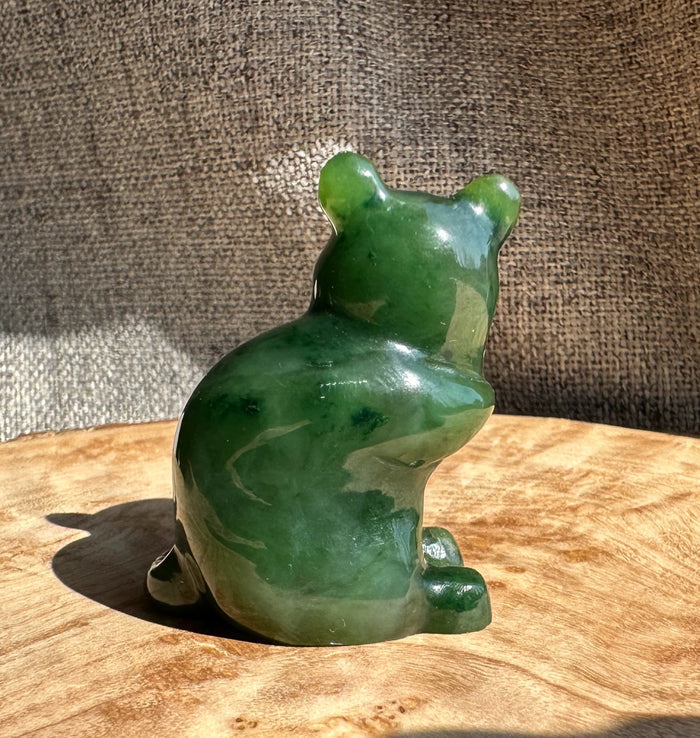 Rear view of a glossy green jade mouse figurine on a wooden table.