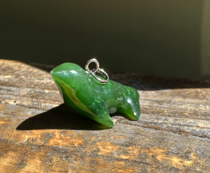 Green jade seal charm with a silver loop resting on weathered wood.