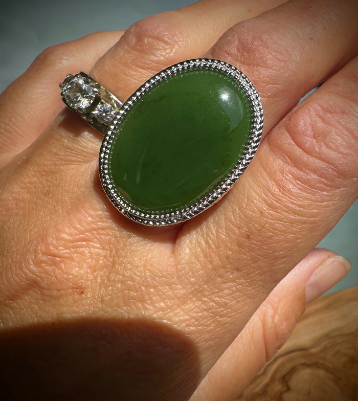 Worn on finger close-up of large green jade ring with silver beaded bezel and side stones