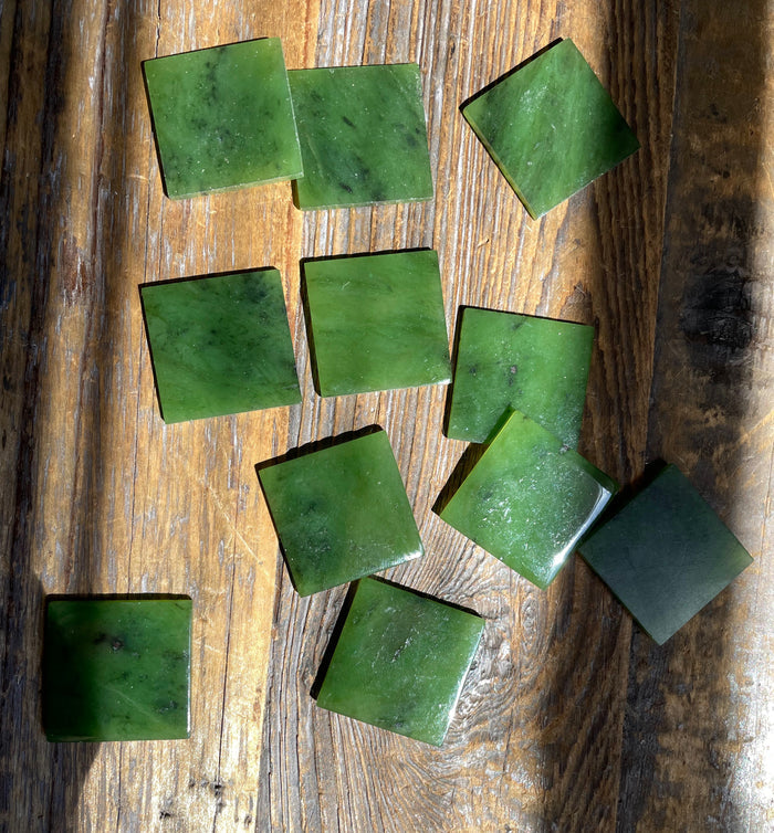 Canadian Jade square cabochons 24.5 x 24.5 mm scattered on a rustic wooden surface
