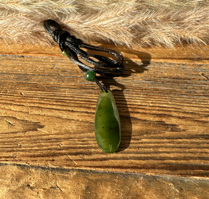 Canadian Jade Teardrop Pendant hanging from knotted black cord with a green bead and wood backdrop