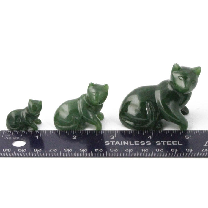 Three dark green cat figurines in size order beside a measuring ruler.