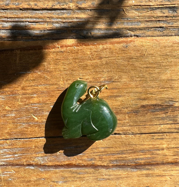 Green dinosaur pendant with a gold loop on a wooden surface