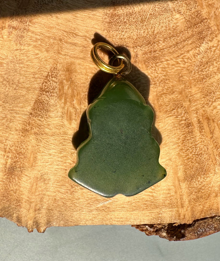 Green jade frog pendant with a gold bail on wood background.