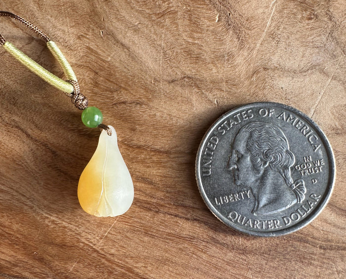 Teardrop honey white nephrite jade pendant with a green bead on a braided cord beside a quarter for scale