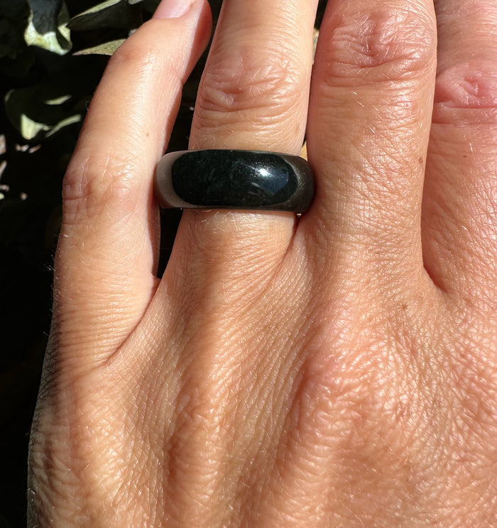 Close up of a dark nephrite jade wide band ring worn on a finger