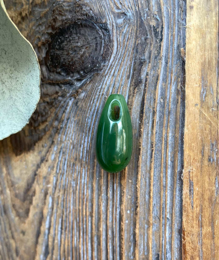Dark green Canadian jade teardrop pendant with a top hole for cord on weathered wood.