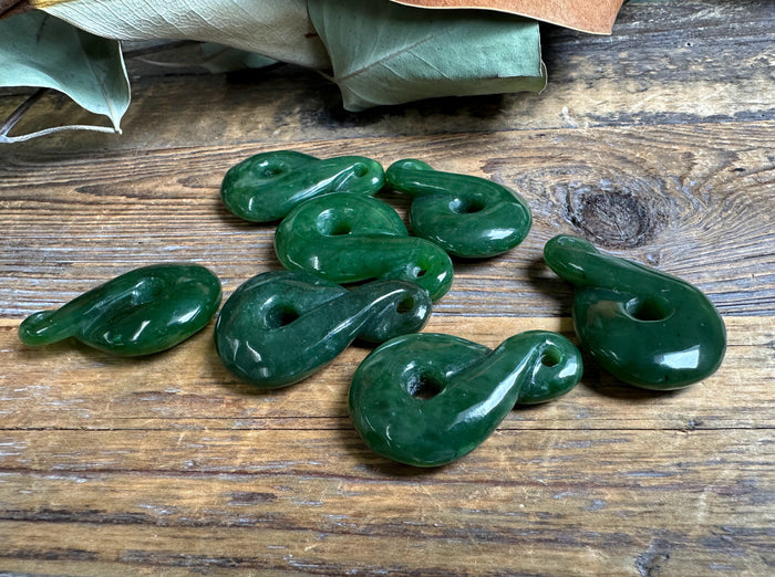 Dark green jade infinity twist pendants in donut shapes scattered on rustic wood.