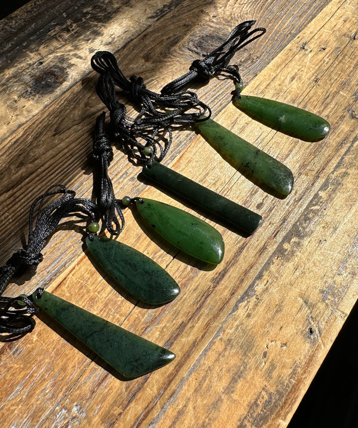 Green jade drop pendants on black cords laid out on a rustic wooden surface