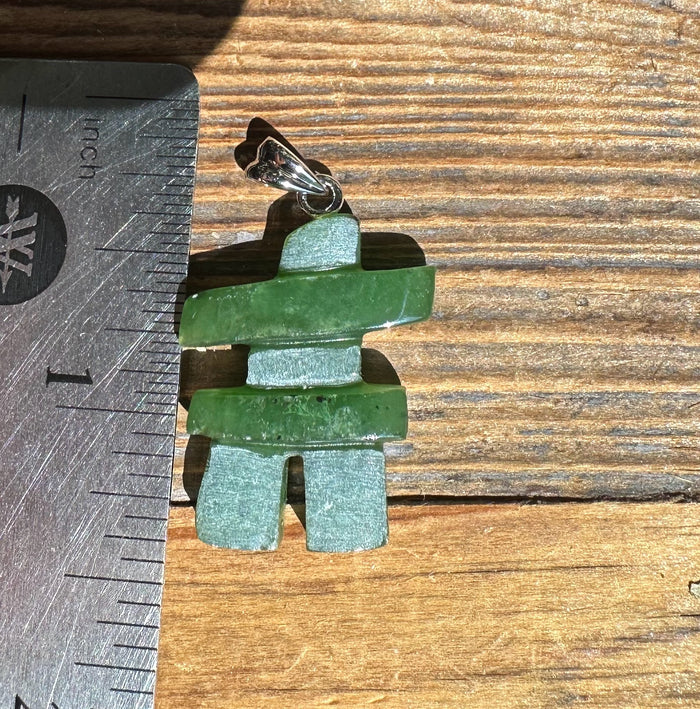 Green jade Inukshuk pendant with a silver bail on a cord beside a ruler for scale.