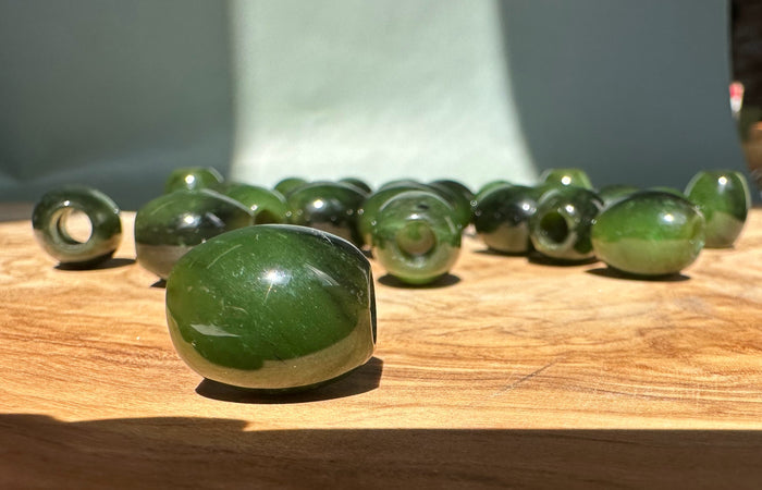 Green jade barrel bead with a central hole resting on a wooden surface