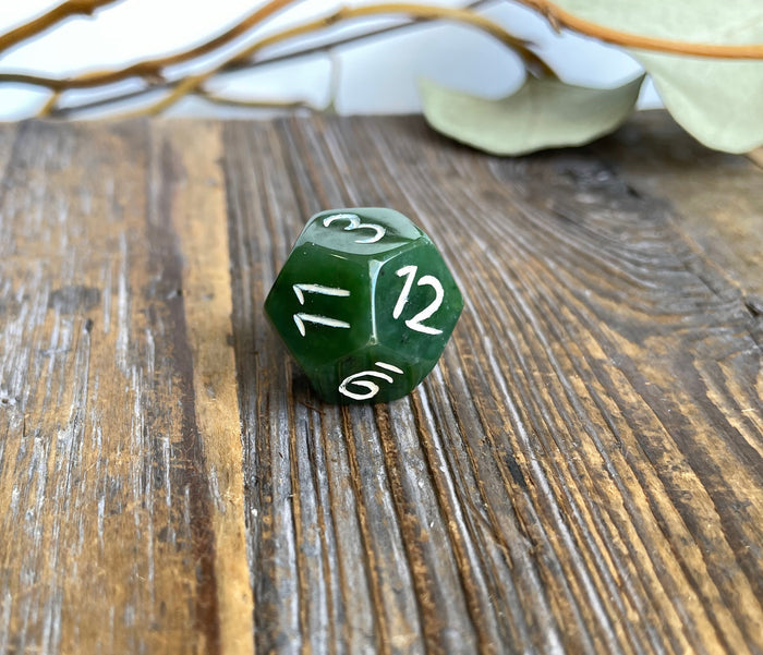 Green jade D12 die with the number 12 facing the camera on a weathered wood background