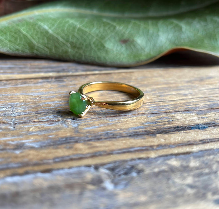 Faceted green jade ring on a gold band resting on a wooden surface
