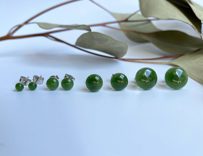 Green jade flat stud earrings in multiple sizes arranged in a row on a white surface