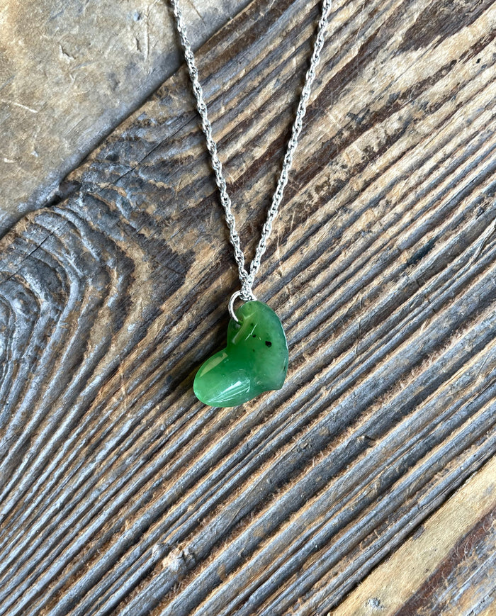 Green jade heart pendant on a silver chain against a rustic wooden surface