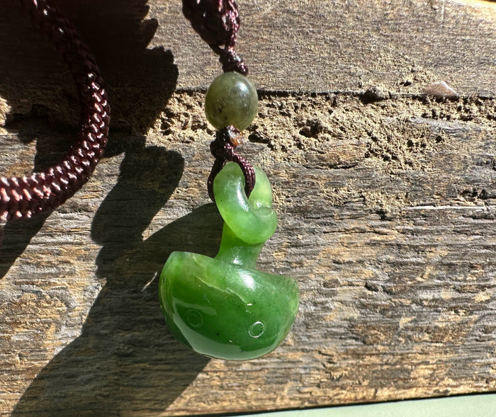 Jade mushroom pendant featuring a round bead on a dark cord against sunlit wood.