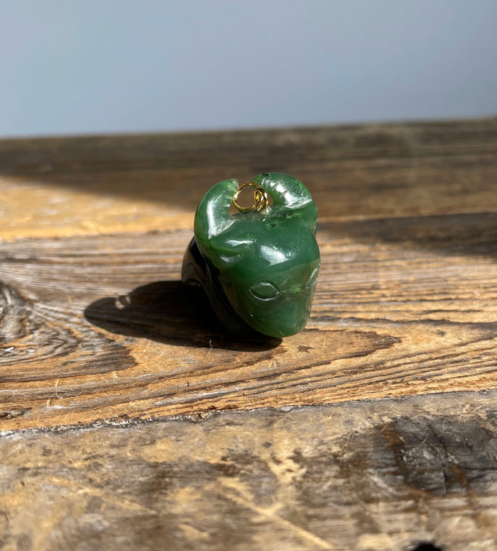 Close-up of green jade ox charm with a gold loop resting on a wooden surface