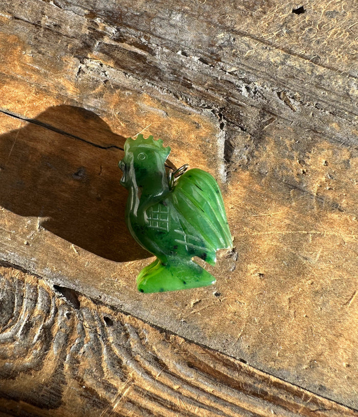 Green jade rooster pendant with a metal loop resting on a wooden surface