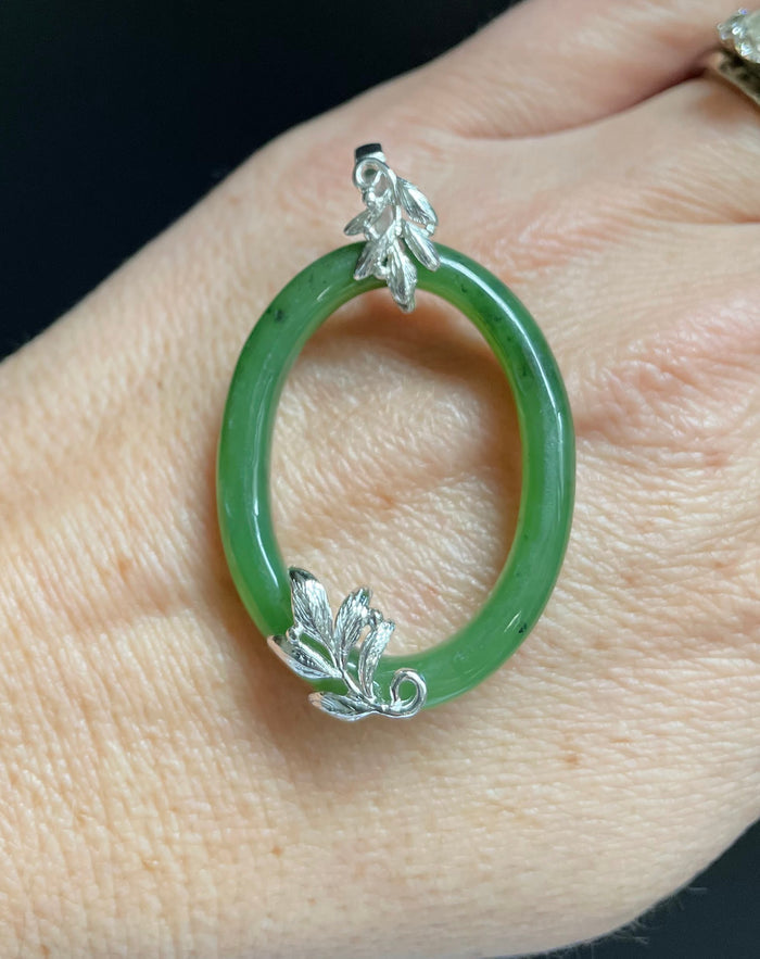 Jade green oval pendant with silver leaf accents worn on a finger.