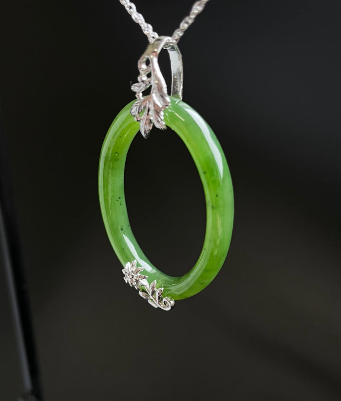 Bright green jade oval pendant in a silver setting with leaf and floral accents at the bail and bottom on a silver chain