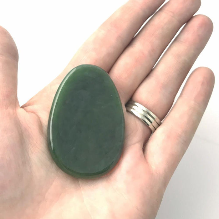 Green jade worry stone held in a hand showing its smooth oval surface