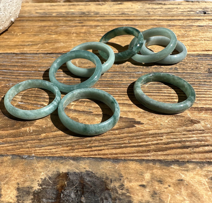 Group of pale to medium green jadeite band rings arranged on a wooden table