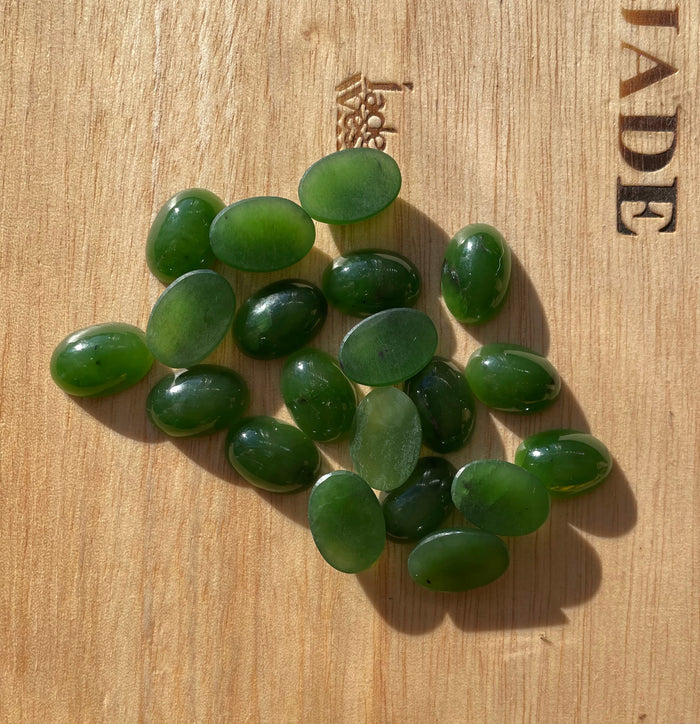 Group of 14x10mm rich green oval Siberian jade cabochons on wood surface