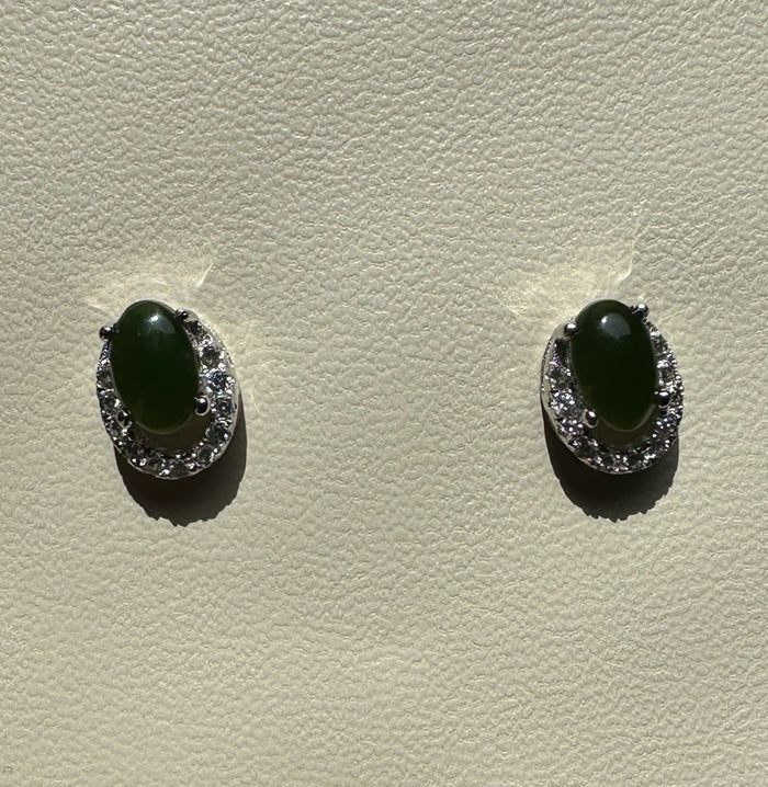 Front view of Silver Jade Studs with green oval jade centers encircled by diamonds on a textured light surface