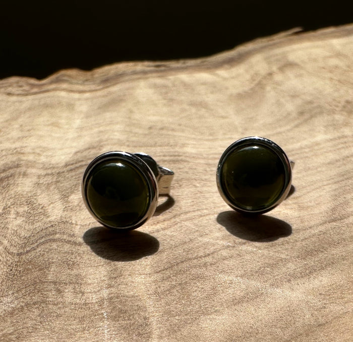 Two round dark green jade stud earrings with silver bezels on wood