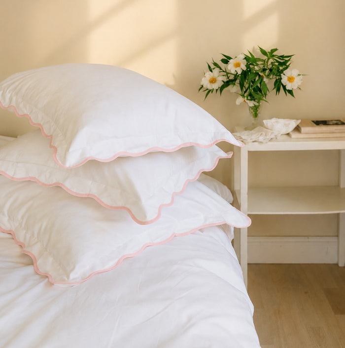 Stack of white pillows with pink trim on a bed in a bedroom setting.