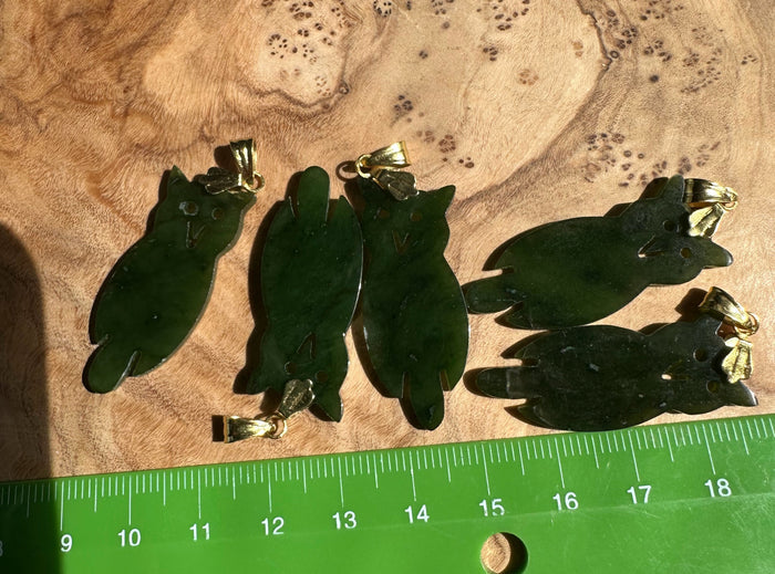 Set of four dark green jade owl pendants with gold bails displayed on wood