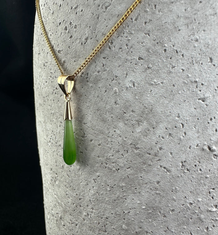 Close-up of gold teardrop pendant with a green gemstone drop on a gold chain