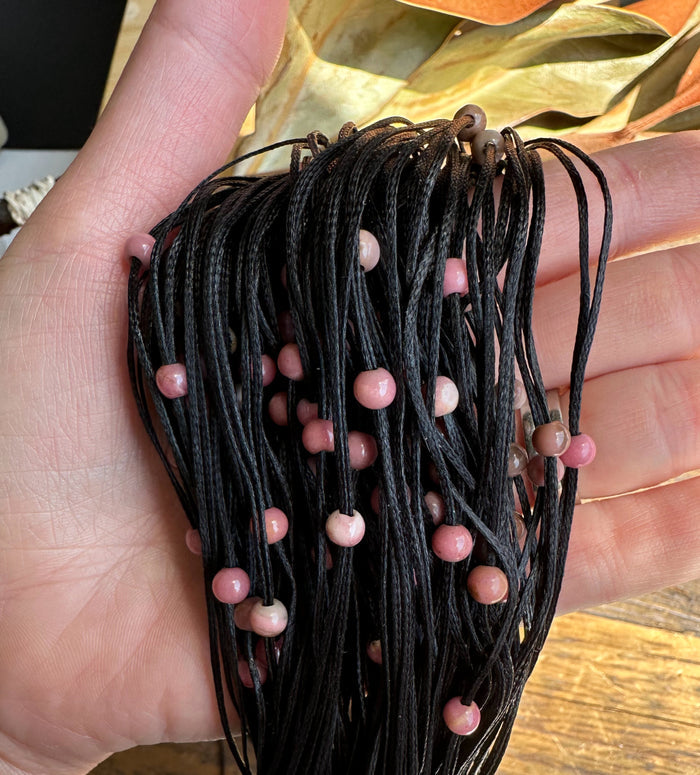 Group of black waxed cord strands with small pink rhodonite beads held in a hand