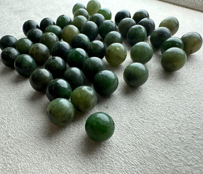 Assorted natural Canadian nephrite jade beads 7-8.5mm mix in greens scattered on a neutral surface