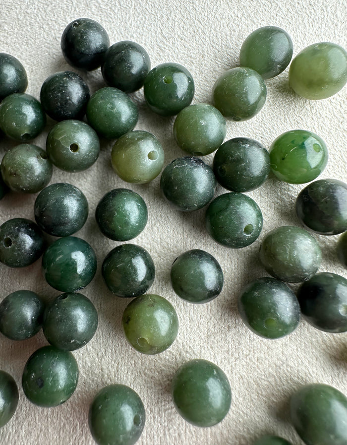 Close up of nephrite jade beads 7-8.5mm with drilled holes in dark to light green hues