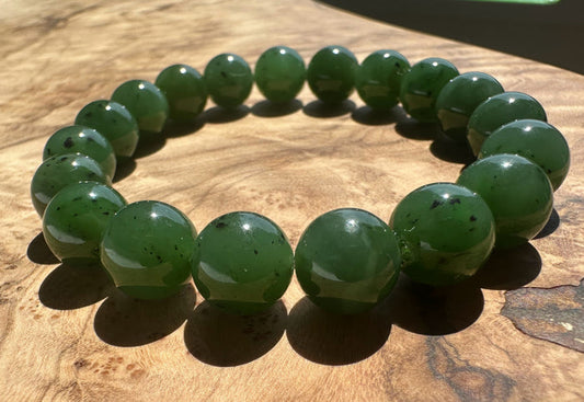 A beaded bracelet made of glossy green jade beads with small dark inclusions, arranged in a circle on a wooden surface.
