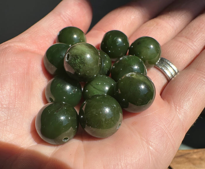 Handful of 14mm Canadian Cassiar jade beads in a palm, each with a drilled hole for stringing