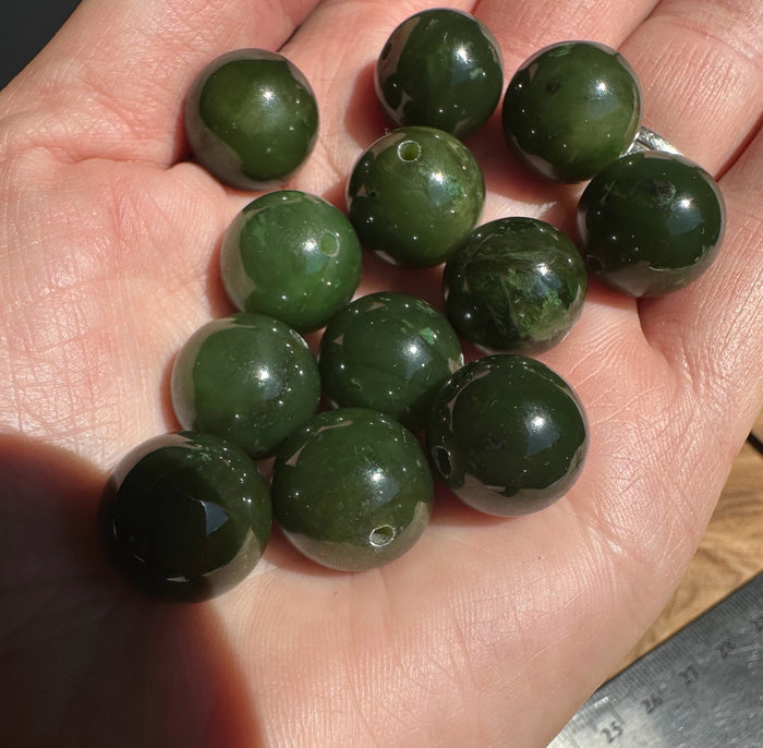 Several 14mm Canadian Cassiar jade beads held in a hand with visible drilled holes for threading